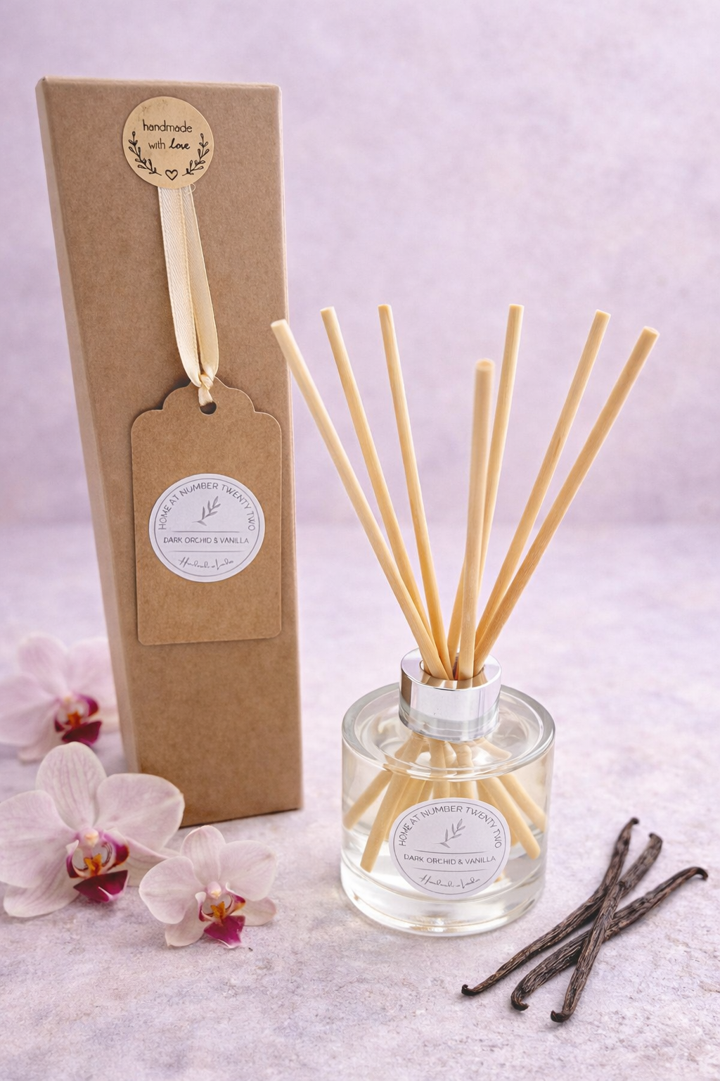 Dark Orchid and Vanilla Reed Diffuser bottle and gift box, alongside dark orchid flowers and sticks of vanilla bean