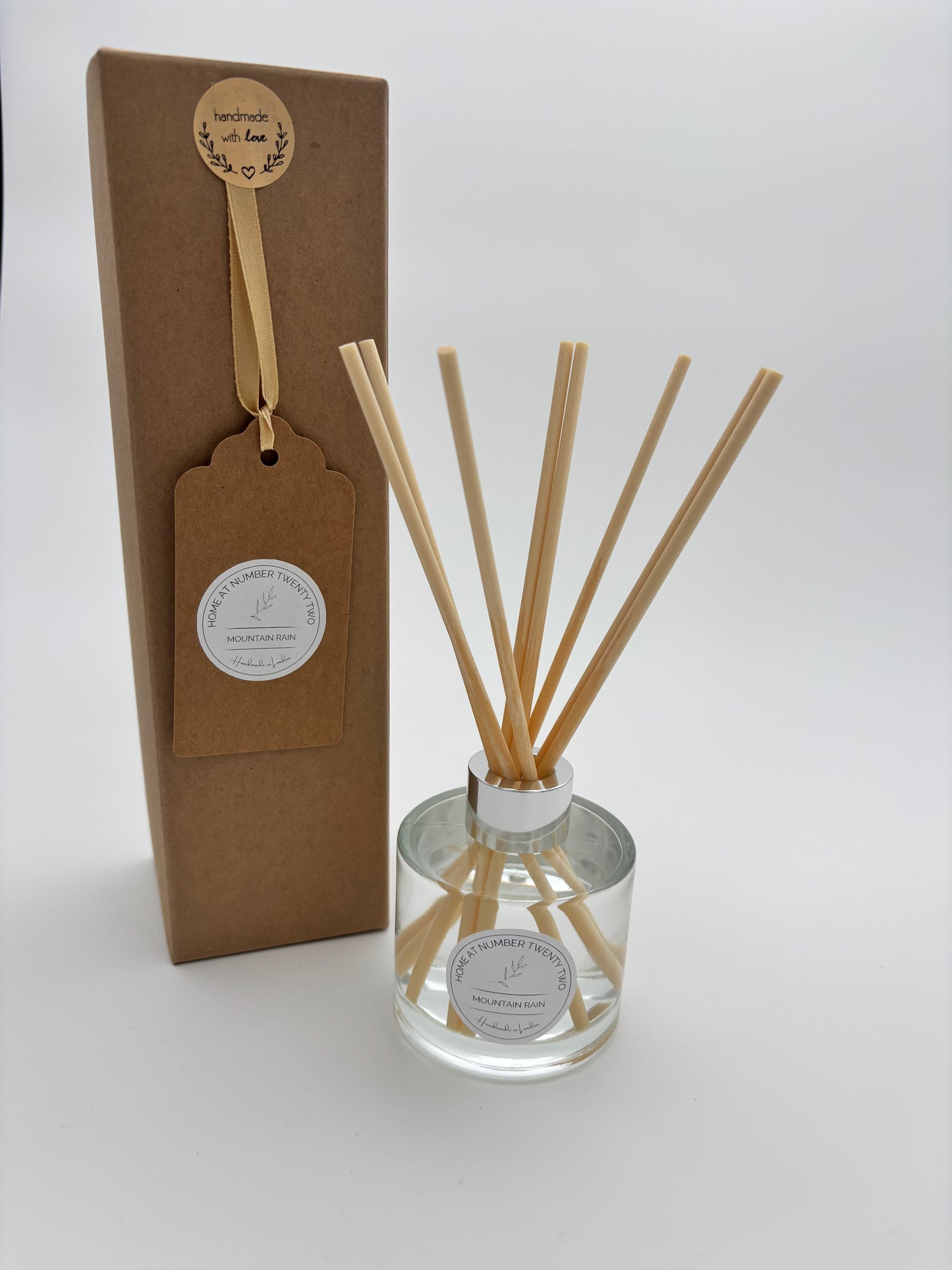 Mountain Rain Reed Diffuser in clear, circular glass bottle with silver cap and natural coloured reeds, alongside Home at Number Twenty Two kraft gift box