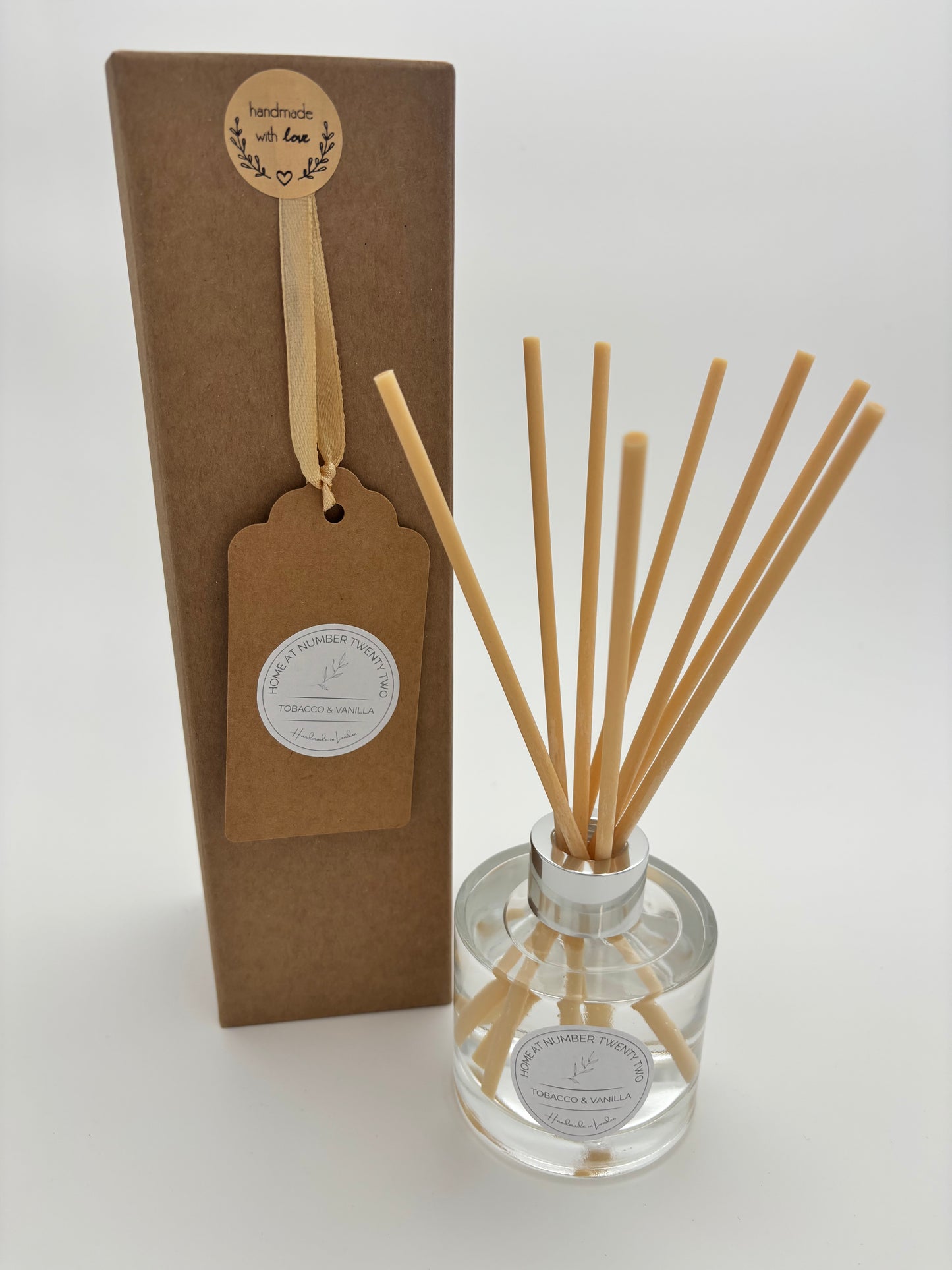 Tobacco and Vanilla Reed Diffuser in clear, glass bottle with silver cap and natural coloured reeds, sat alongside Home at Number Twenty Two branded kraft gift box