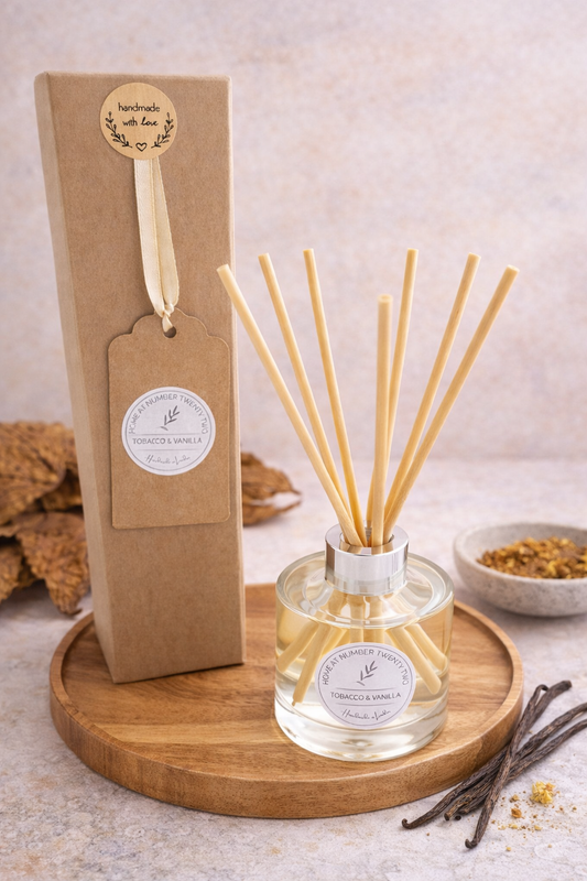 Tobacco and Vanilla Reed Diffuser, sat on circular wooden tray with tobacco leaves in the background and vanilla pod seeds