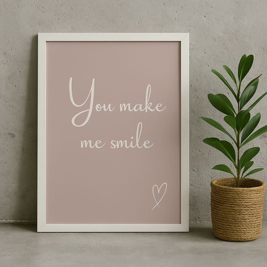 Framed print with 'You make me smile' text on a pink background, next to a potted plant.
