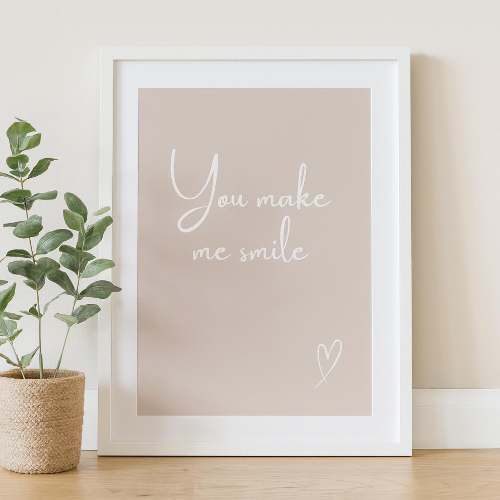 Framed print with 'You make me smile' text on a beige background, placed indoors with a plant.