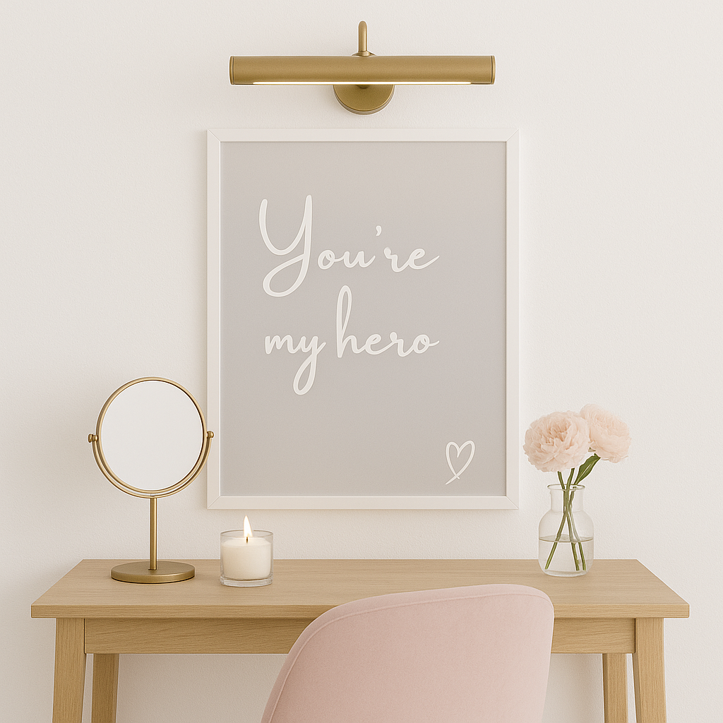 Decorative setup with a framed quote 'you're my hero'', mirror, candle, and flowers on a wooden table.